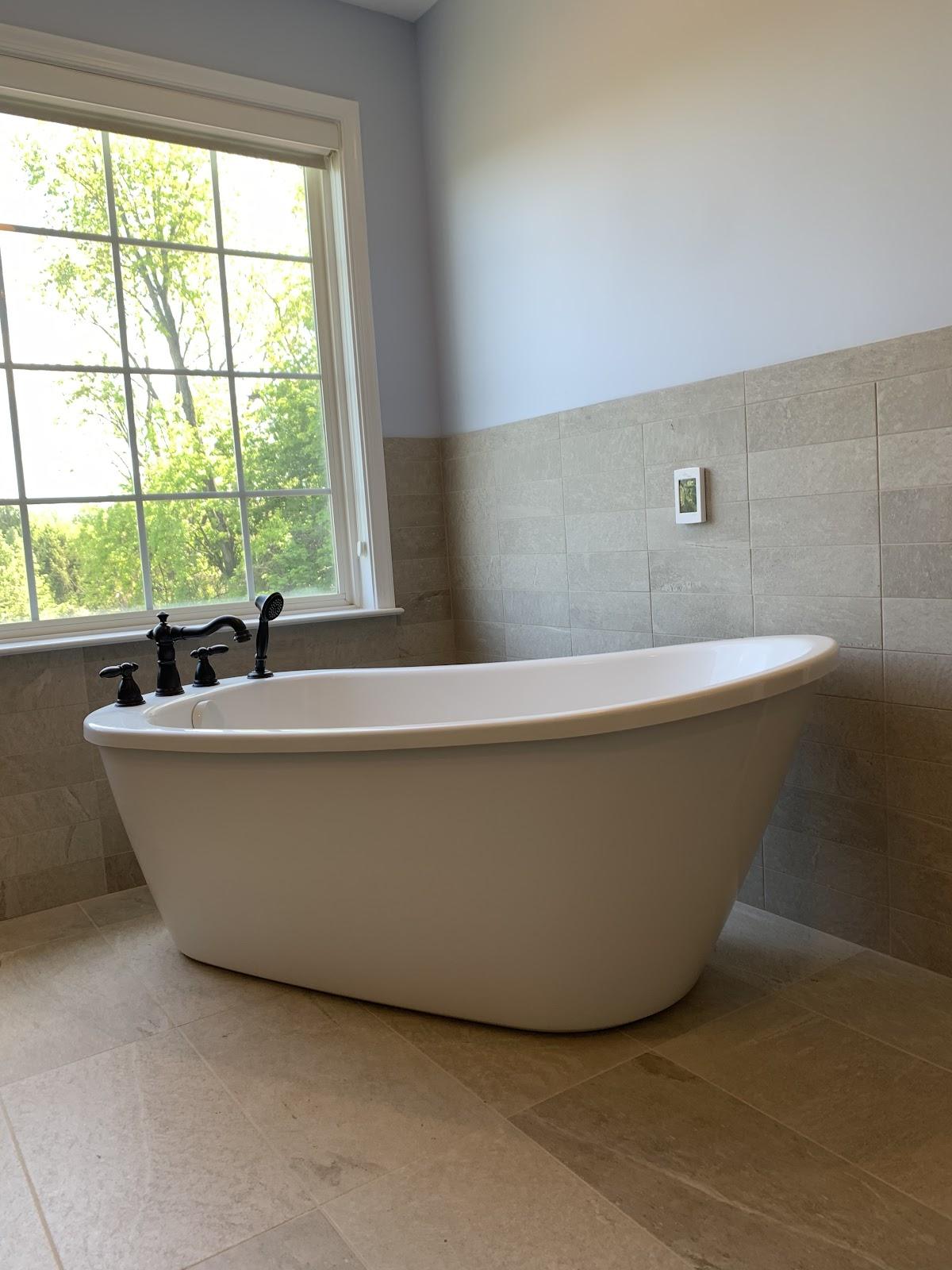 Freestanding tub installed by a bright window with a bronze faucet
